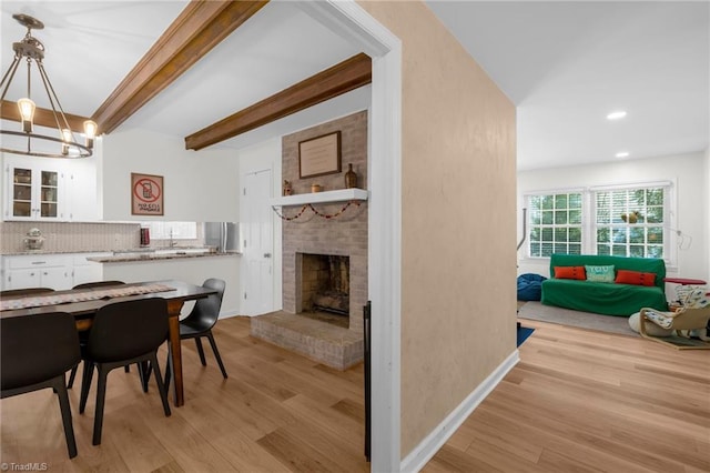 dining area featuring a brick fireplace, beam ceiling, recessed lighting, light wood finished floors, and a notable chandelier