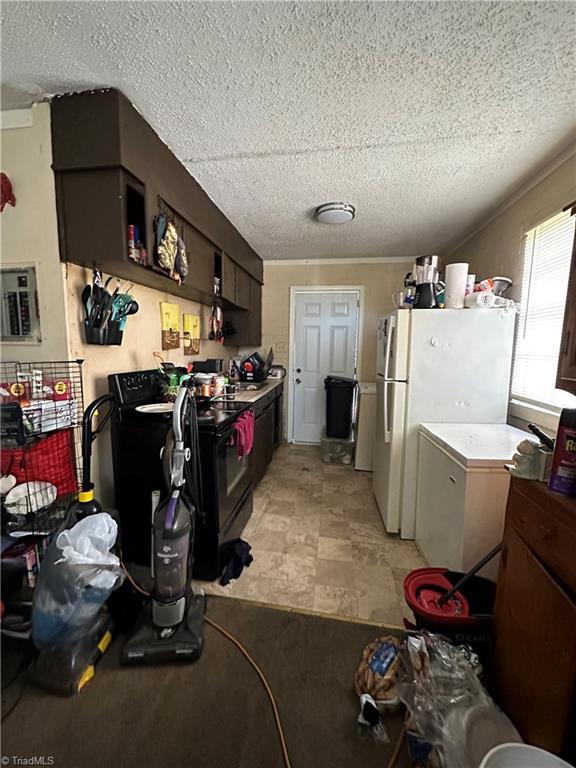 kitchen featuring electric panel, a textured ceiling, black range with electric stovetop, and freestanding refrigerator