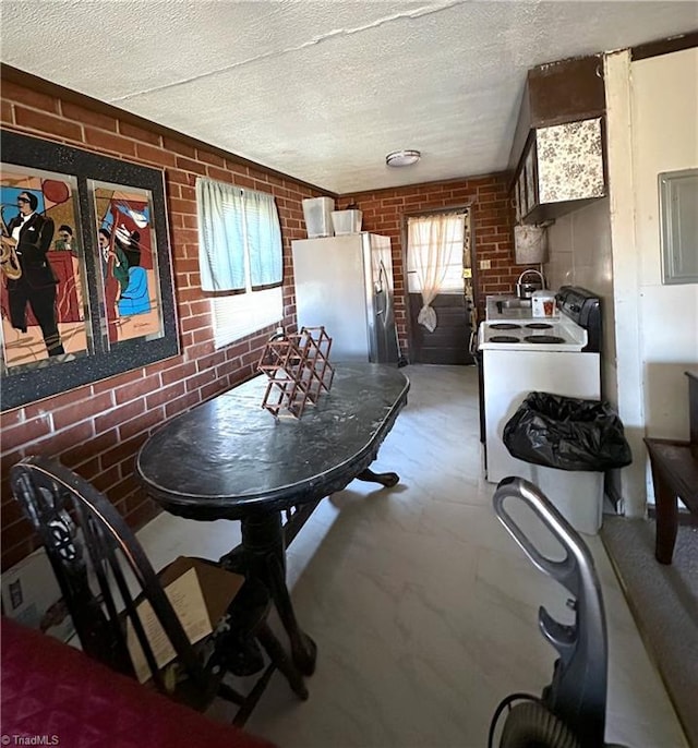 kitchen featuring a textured ceiling, brick wall, washer / clothes dryer, and freestanding refrigerator