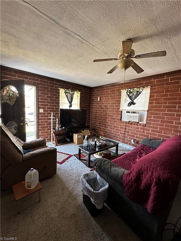 living room with brick wall, carpet, ceiling fan, and a textured ceiling