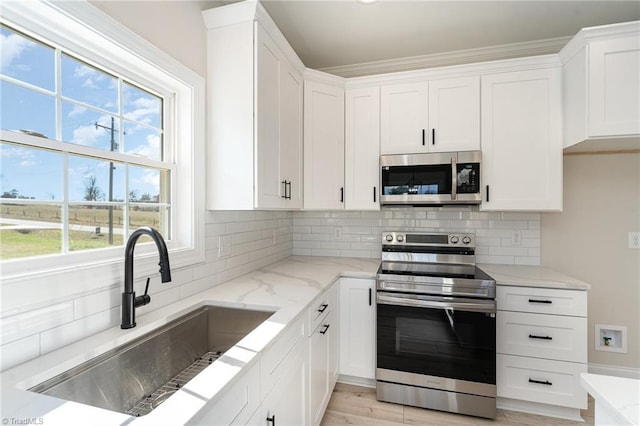 kitchen with tasteful backsplash, light stone countertops, stainless steel appliances, white cabinetry, and a sink