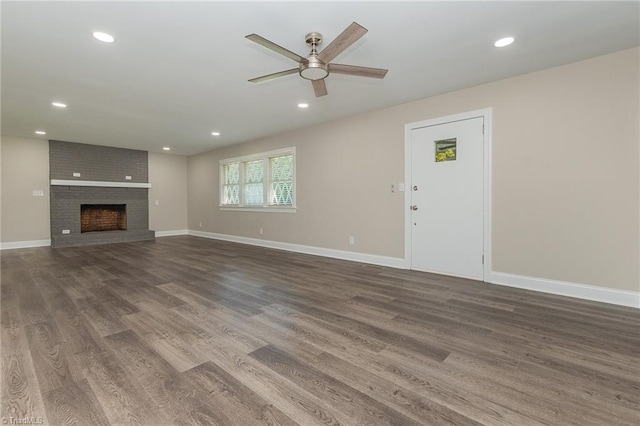 unfurnished living room with a brick fireplace, ceiling fan, and dark hardwood / wood-style floors