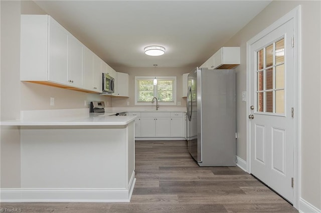kitchen featuring sink, white cabinets, light hardwood / wood-style flooring, kitchen peninsula, and appliances with stainless steel finishes