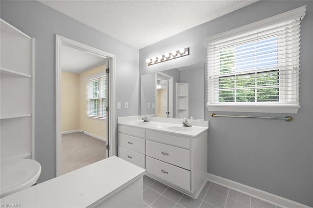 bathroom with healthy amount of natural light, double vanity, a textured ceiling, baseboards, and tile patterned flooring