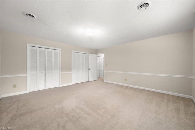 unfurnished bedroom featuring multiple closets, carpet flooring, baseboards, and a textured ceiling