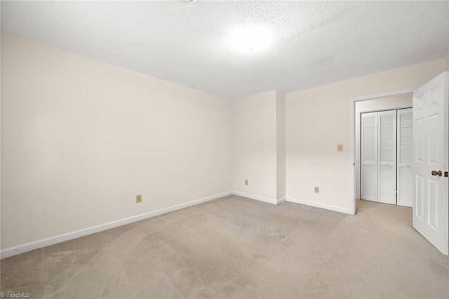unfurnished bedroom featuring light colored carpet, baseboards, a textured ceiling, and a closet
