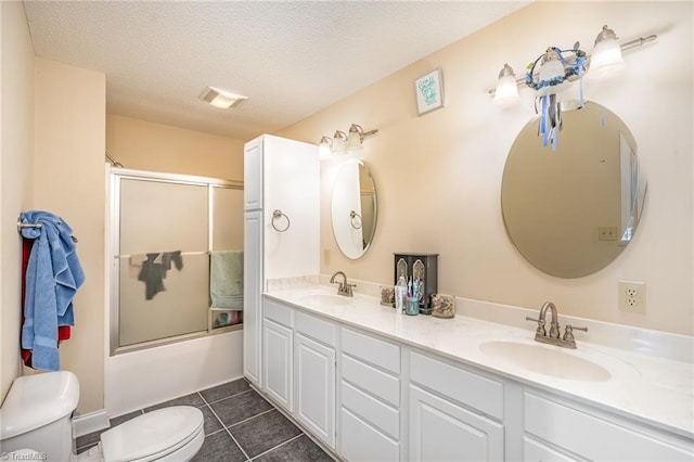 full bathroom with bath / shower combo with glass door, tile patterned flooring, vanity, toilet, and a textured ceiling