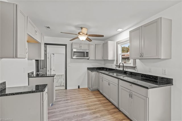 kitchen featuring dark stone counters, sink, gray cabinetry, ceiling fan, and light wood-type flooring