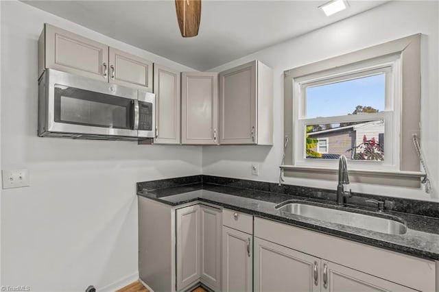 kitchen featuring dark stone counters, hardwood / wood-style floors, sink, gray cabinets, and ceiling fan