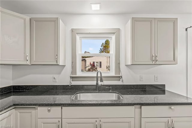 kitchen with dark stone countertops, gray cabinetry, and sink