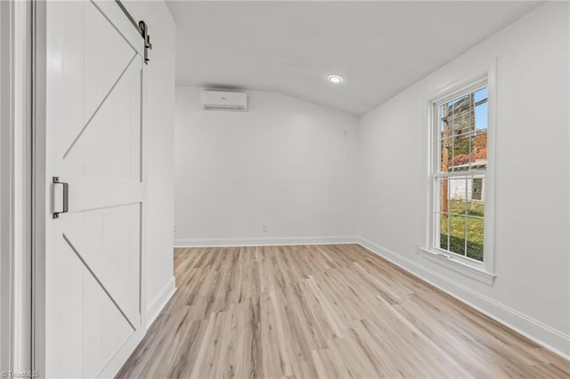 unfurnished room with light hardwood / wood-style flooring, a barn door, and vaulted ceiling