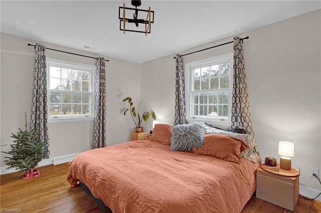 bedroom with hardwood / wood-style floors, an inviting chandelier, and multiple windows