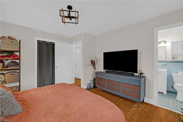 bedroom with connected bathroom, an inviting chandelier, light hardwood / wood-style flooring, and tile walls