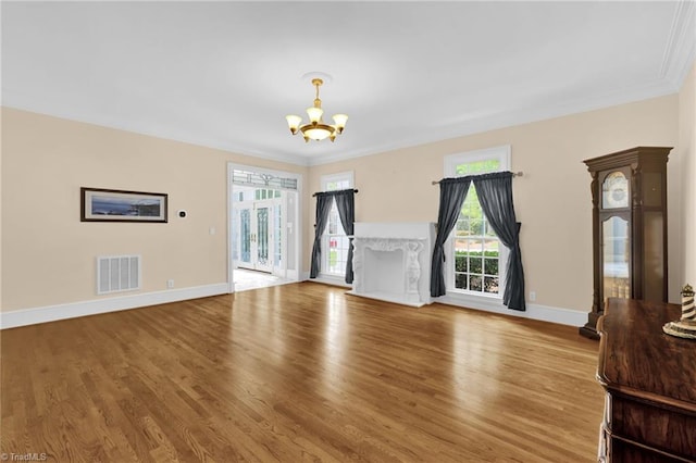 unfurnished living room with plenty of natural light, visible vents, wood finished floors, baseboards, and a notable chandelier