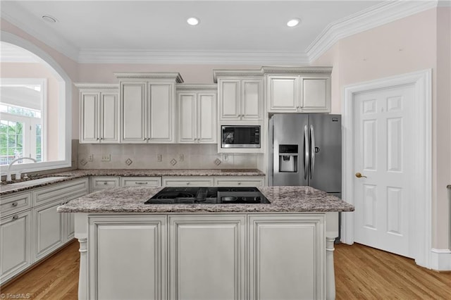 kitchen featuring appliances with stainless steel finishes, a sink, light wood-style flooring, a center island, and backsplash
