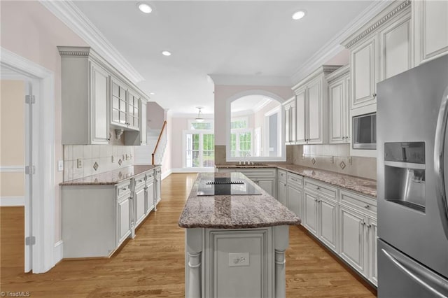 kitchen featuring crown molding, appliances with stainless steel finishes, light wood finished floors, decorative backsplash, and a kitchen island