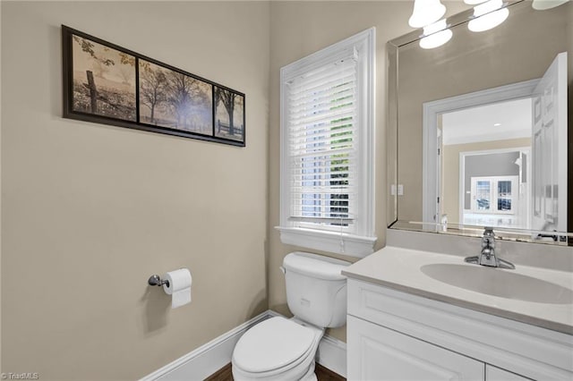 half bathroom featuring vanity, baseboards, and toilet