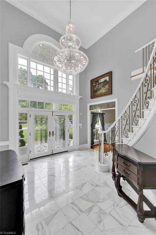 entrance foyer with ornamental molding, a healthy amount of sunlight, stairway, and a towering ceiling