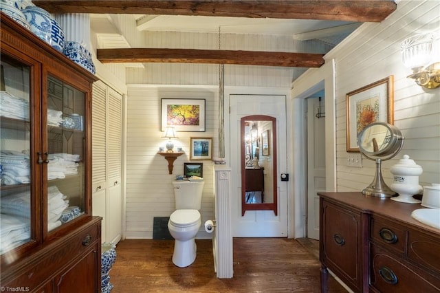 bathroom featuring wood walls, toilet, and beamed ceiling