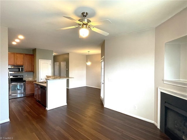 kitchen with dark wood-style floors, brown cabinets, a fireplace, appliances with stainless steel finishes, and a ceiling fan