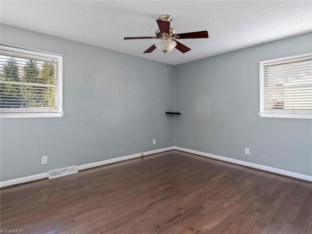 empty room featuring baseboards, visible vents, dark wood-style flooring, and a textured ceiling