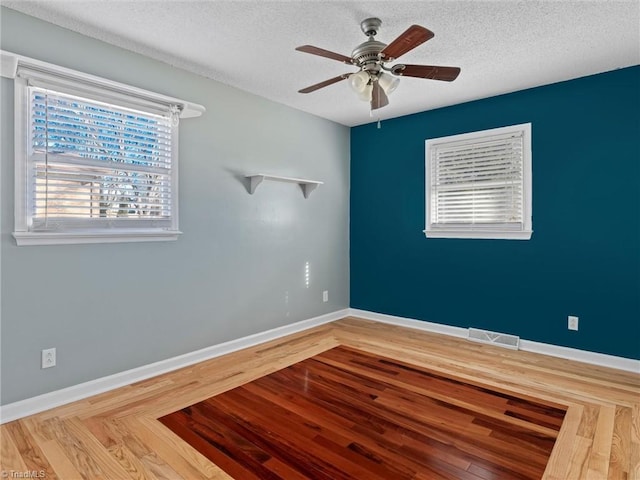 empty room with a ceiling fan, wood finished floors, baseboards, visible vents, and a textured ceiling