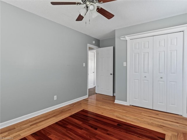 unfurnished bedroom featuring wood finished floors, baseboards, a closet, and a textured ceiling