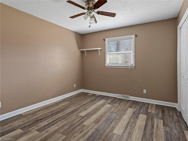 empty room with a textured ceiling, wood finished floors, baseboards, and ceiling fan