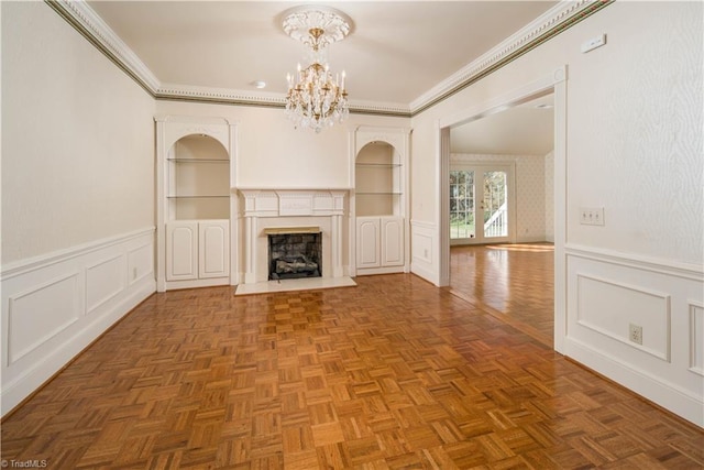 unfurnished living room with parquet floors, built in features, ornamental molding, and an inviting chandelier