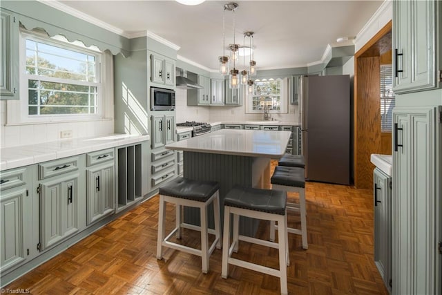 kitchen featuring wall chimney range hood, a kitchen island, ornamental molding, dark parquet flooring, and stainless steel appliances