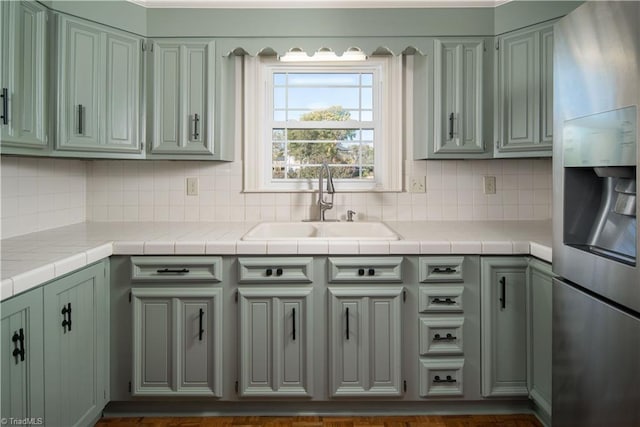 kitchen with sink, backsplash, stainless steel fridge with ice dispenser, and tile counters