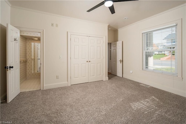 unfurnished bedroom featuring ensuite bath, ornamental molding, a closet, ceiling fan, and carpet