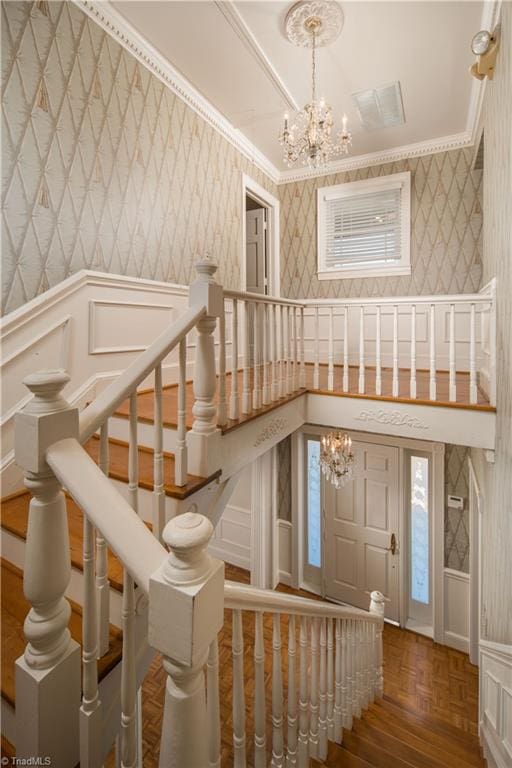 stairs featuring crown molding, parquet floors, and a chandelier