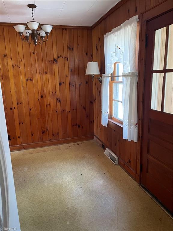 unfurnished dining area with wood walls, baseboards, visible vents, and a notable chandelier