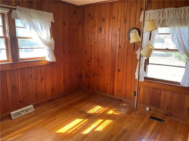 unfurnished room with wood walls, visible vents, and wood finished floors