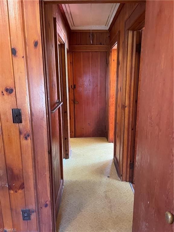 corridor with light carpet, wood walls, and attic access