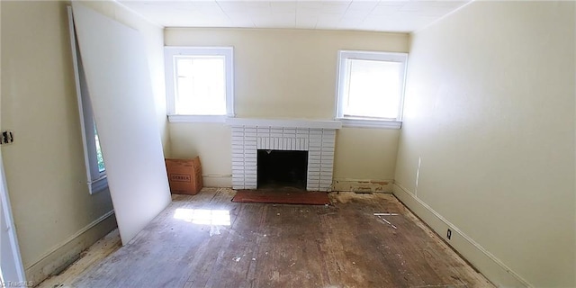 unfurnished living room featuring wood finished floors, a brick fireplace, and baseboards