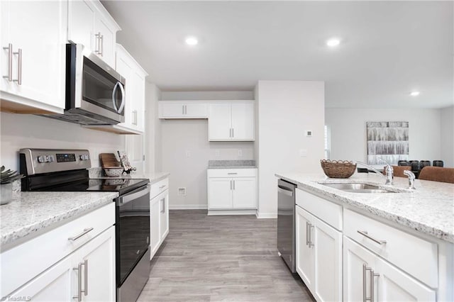 kitchen with appliances with stainless steel finishes, white cabinetry, sink, light stone countertops, and light hardwood / wood-style flooring