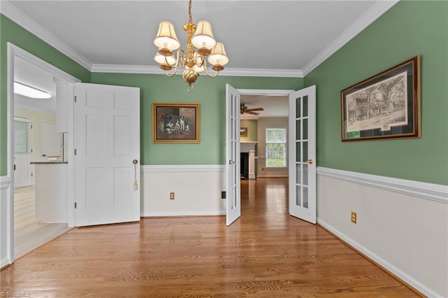 unfurnished dining area featuring french doors, a chandelier, ornamental molding, and wood finished floors