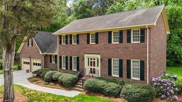 colonial home featuring central AC unit, a garage, brick siding, concrete driveway, and a shingled roof