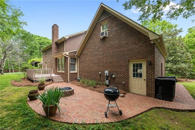 rear view of property with a chimney, a lawn, a deck, brick siding, and a fire pit