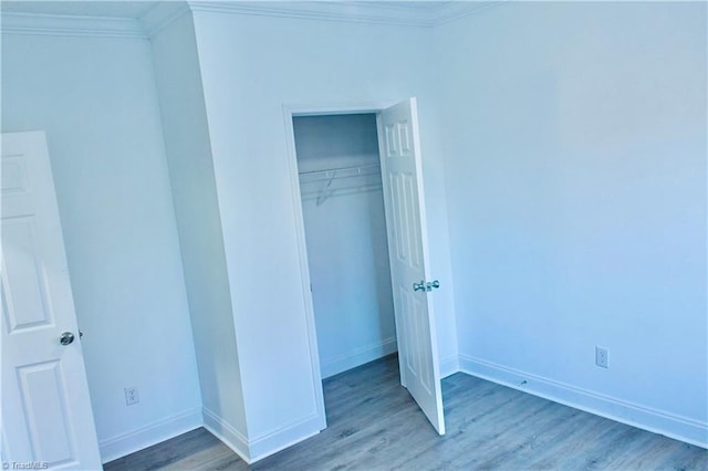 unfurnished bedroom with crown molding, a closet, and hardwood / wood-style flooring