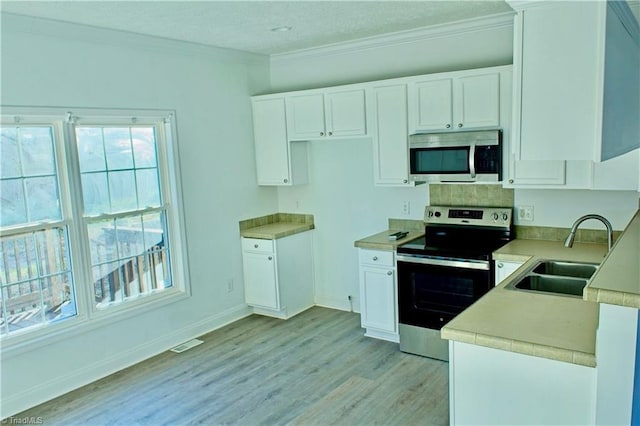 kitchen with appliances with stainless steel finishes, light wood-type flooring, crown molding, sink, and white cabinets