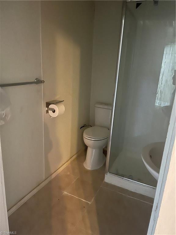 bathroom featuring a shower with door, toilet, and tile patterned floors