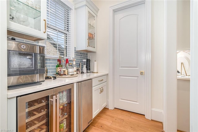 bar featuring decorative backsplash, beverage cooler, a bar, and light wood-style flooring