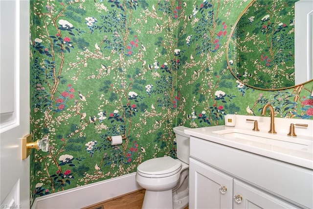 half bathroom featuring toilet, wallpapered walls, vanity, and wood finished floors