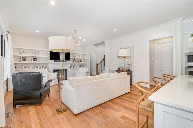 living room featuring stairs, crown molding, light wood-style flooring, and a fireplace