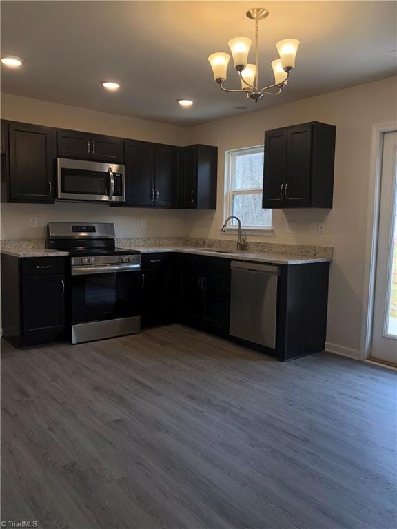 kitchen featuring pendant lighting, stainless steel appliances, light wood-style floors, a sink, and baseboards