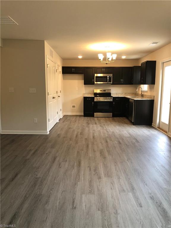 kitchen featuring dark cabinets, wood finished floors, a sink, light countertops, and appliances with stainless steel finishes