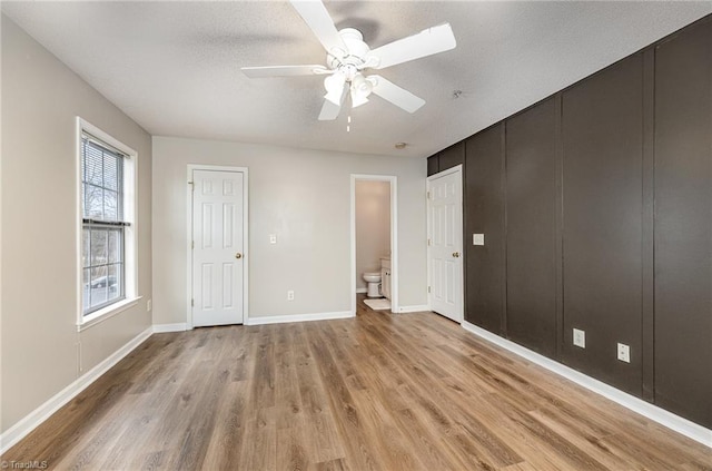 unfurnished bedroom featuring light wood-style flooring, ensuite bathroom, a textured ceiling, baseboards, and ceiling fan